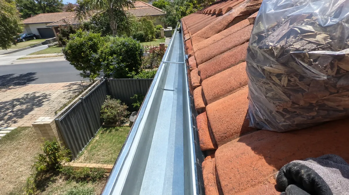 Gutter cleaning Perth: freshly cleaned galvanised gutter along a tile roof with a bag of removed leaf litter