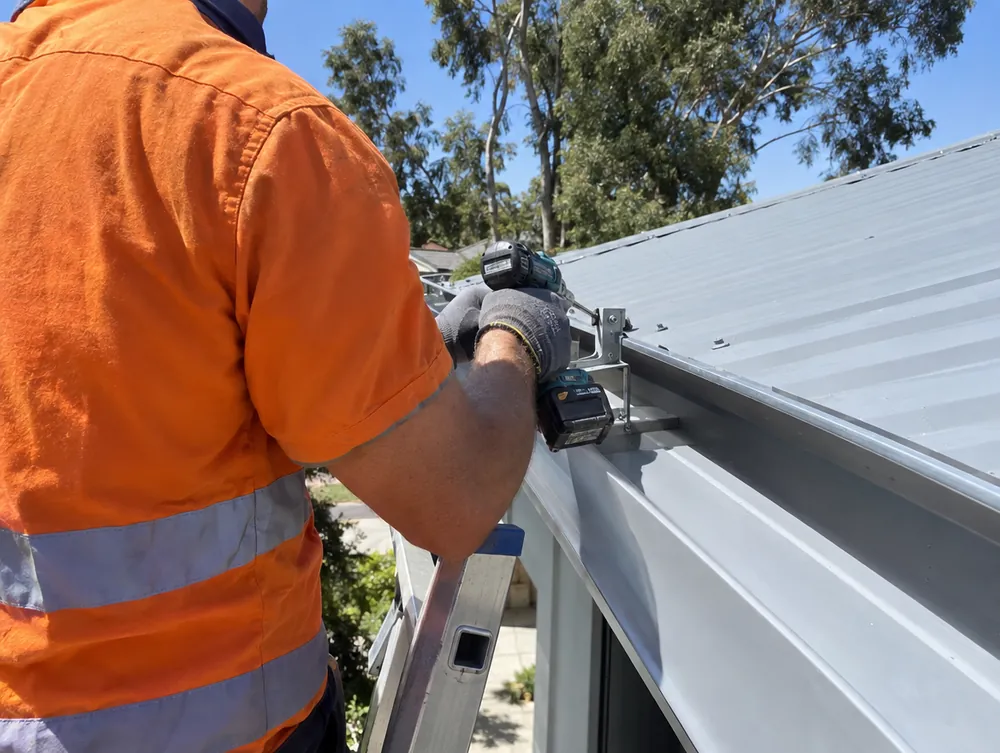 Gutter repair Perth: tradesman in hi-vis fixing a gutter bracket with a cordless drill on a Colorbond roof
